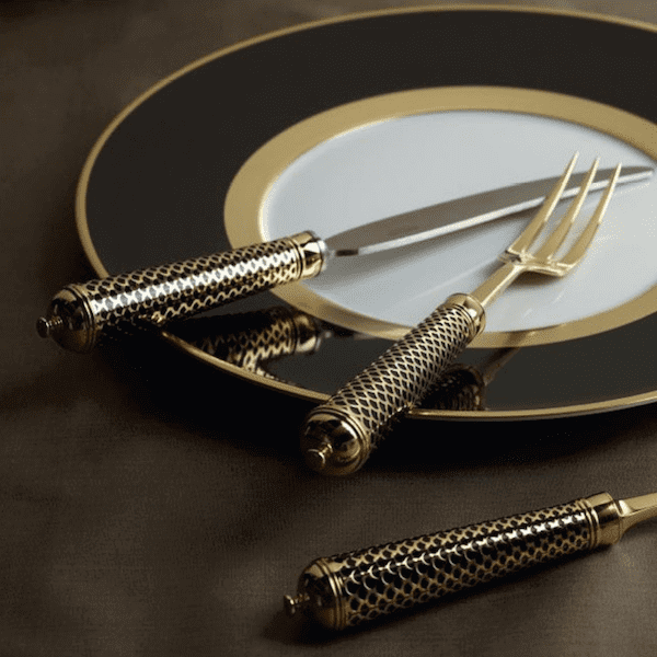 Ercuis gold-patterned French cutlery set displayed on an elegant black and gold dinner plate